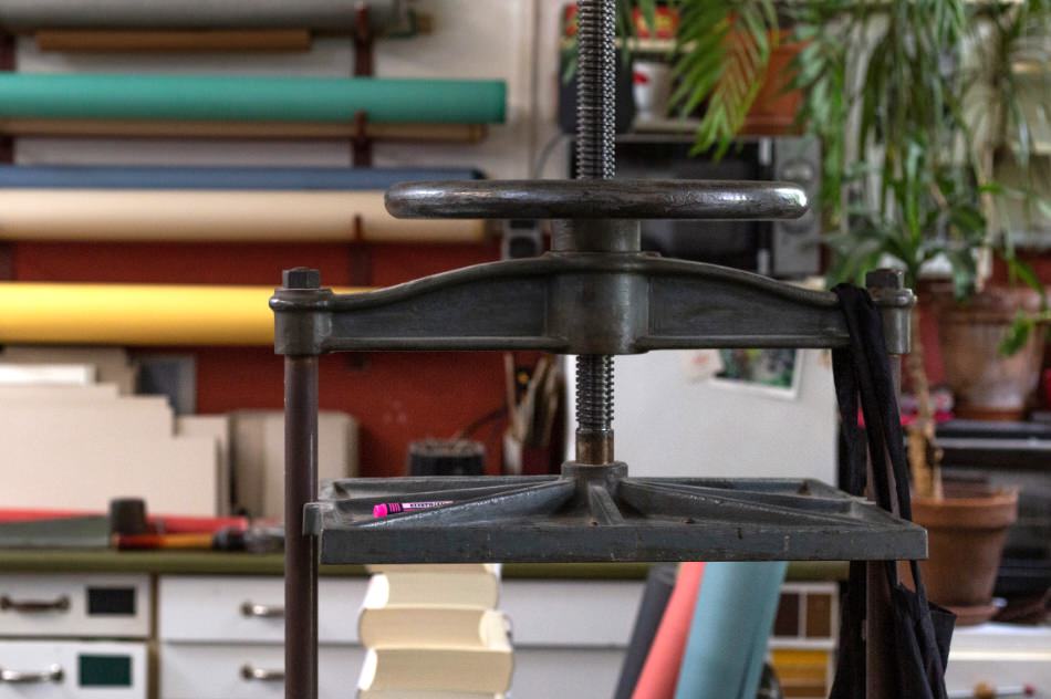 Traditionelle Buchpresse in einer Buchbinderei mit farbigen Papierrollen im Hintergrund